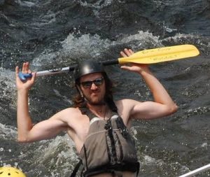 A shirtless rafting guide holding up a paddle during one of the Colorado river rafting day trips