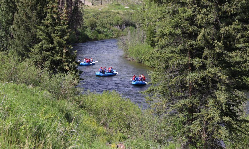 Three KODI Rafting inflatable boats with people on them while rafting down a destination river.