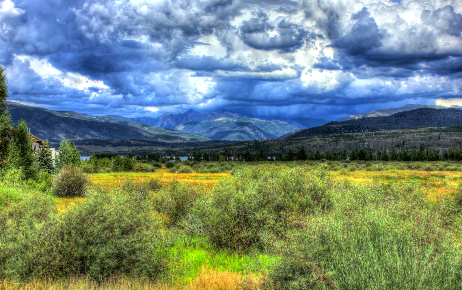 View of a KODI Rafting destination landscape with a green field, mountains, and cloudy sky.