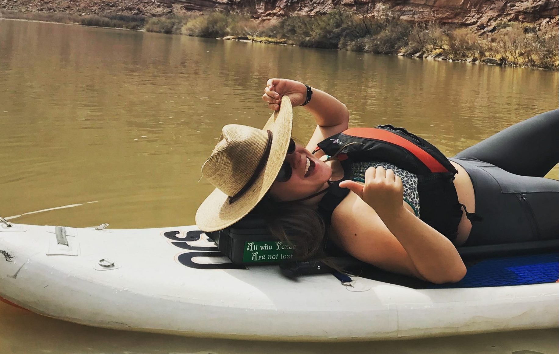 A smiling girl in a straw hat is lying on a white SUP board provided by KODI Rafting.