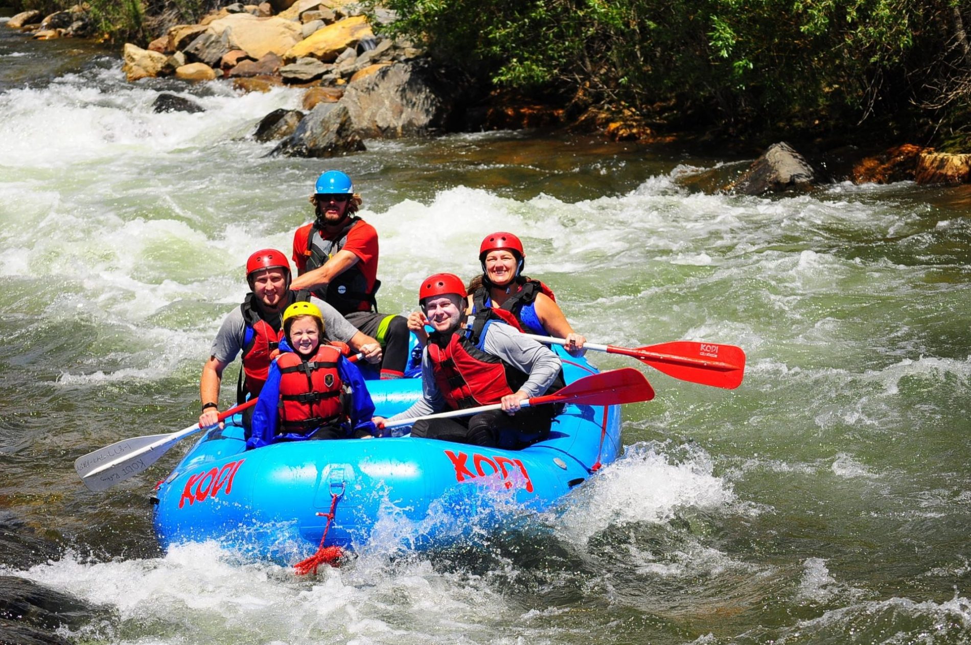 KODI Rafting's blue inflatable boat on a tour with passengers in life jackets and helmets.