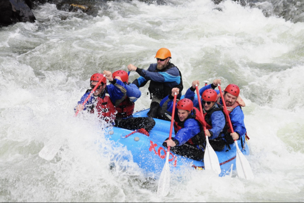 Group and raft guide maneuvering bumpy river rapids on an advanced whitewater rafting adventure 