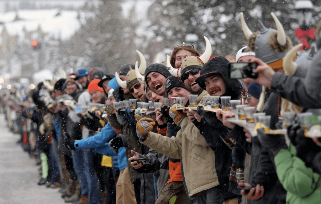 Ullr fest participants hold up skis and cups promoting snow-based and whitewater rafting activities