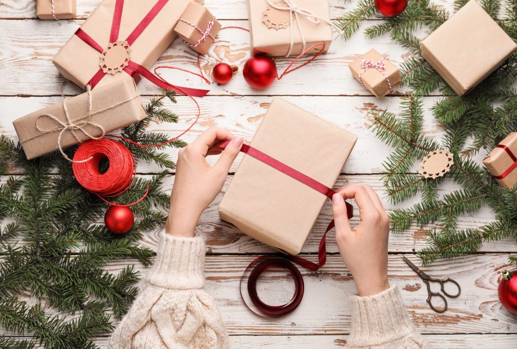 A woman hand wraps a gift purchased from KODI Rafting in a New Year's wrap with a red ribbon.