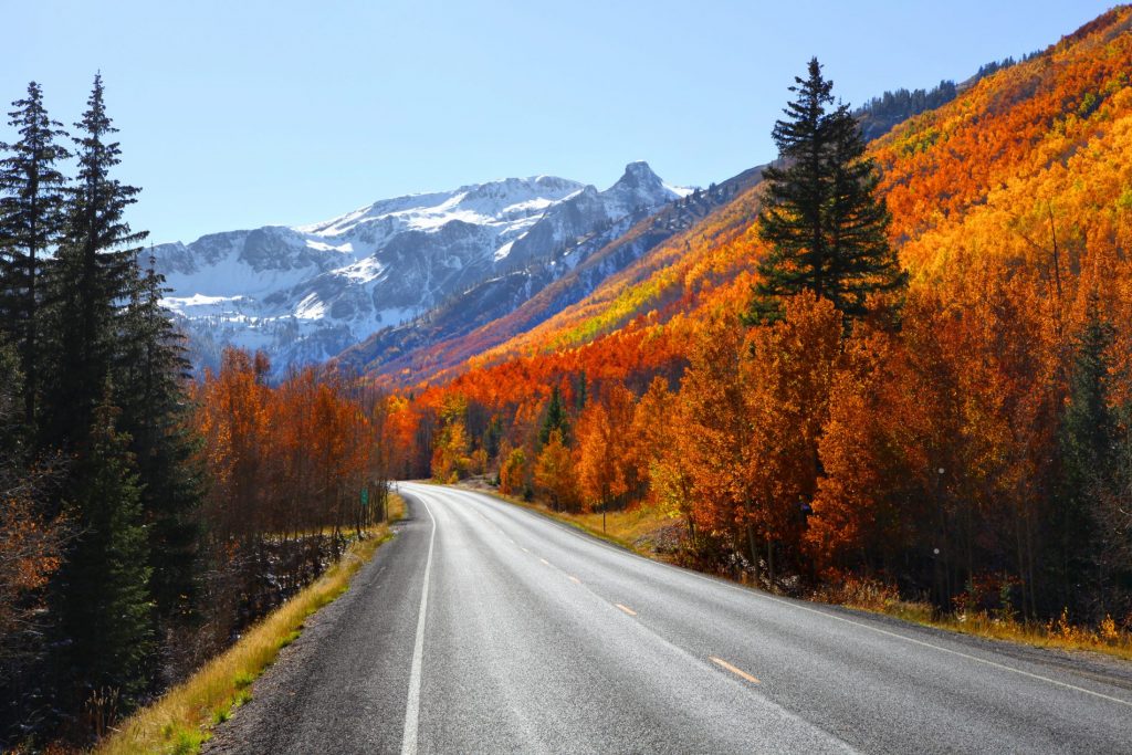 A mountainous landscape with red Aspen trees along a tarmac road for driving to kayak river trips